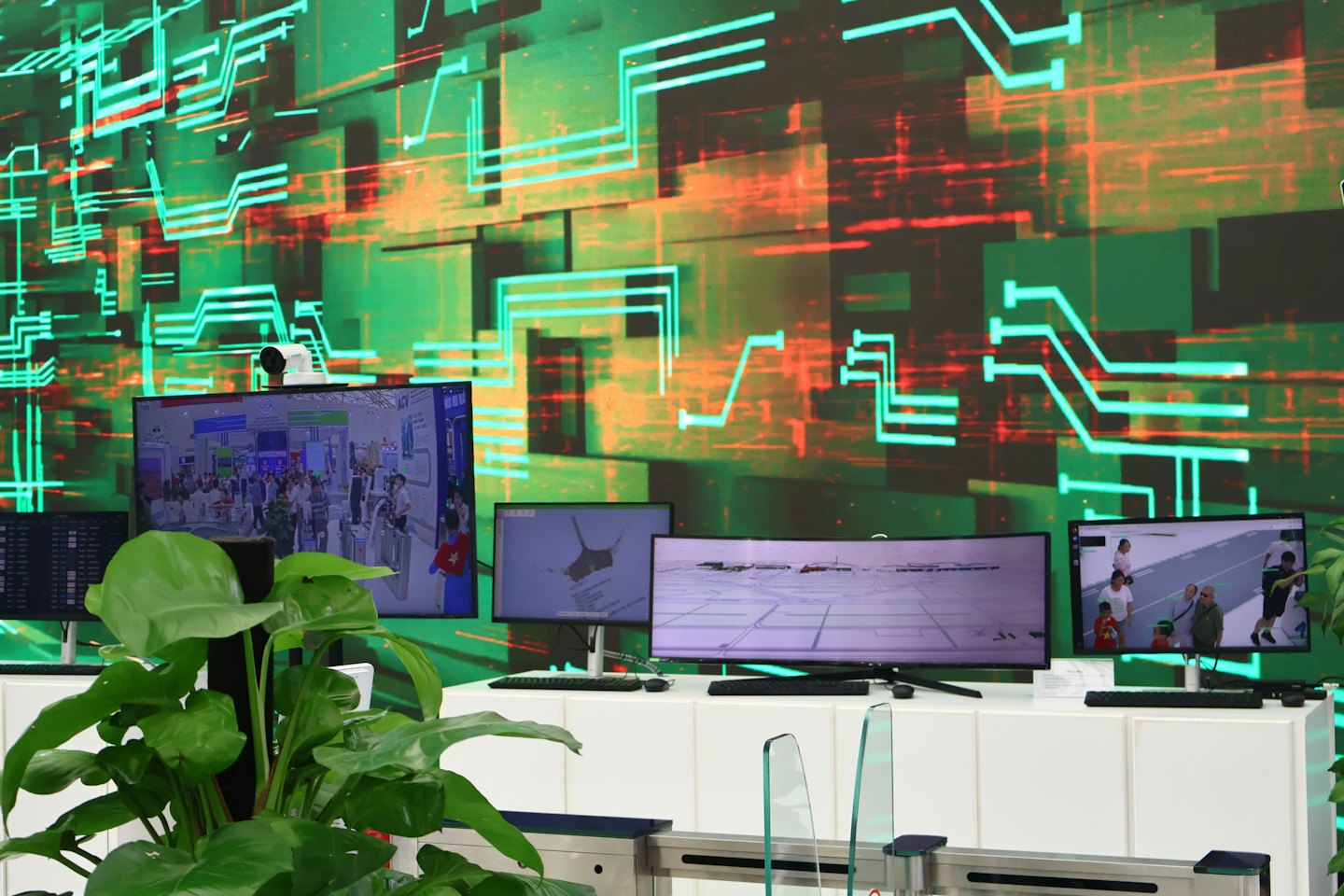 Multiple digital screens display security footage and maps in a control room.